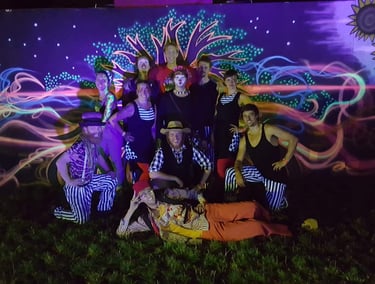 A troupe of circus performers in colourful costumes posing before a vibrant neon projection mural.