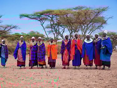 Maasai women in traditional vibrant blue and red shuka robes and beaded jewelry standing in a row.