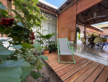 A green striped deck chair sits on a wooden patio in a tropical garden patio setting.