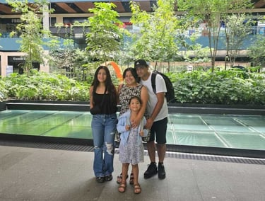 A happy family posing together in a modern outdoor shopping center with lush green plants.
