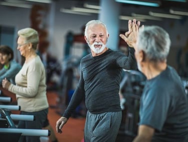 Idosos se exercitam na academia e celebram com um high five, mostrando energia e bem-estar.