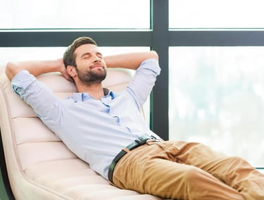 A relaxed man leaning back on a lounge chair with eyes closed, enjoying a break in a modern office.