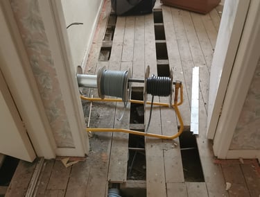 Electrical cable reels on a stand over exposed wooden floorboards during a home renovation.