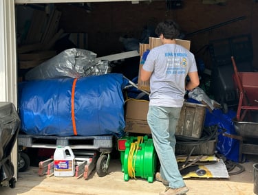 Professional junk removal worker clearing out a cluttered garage filled with boxes and debris.