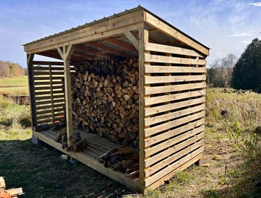 a wooden storage shed with logs stacked on top of it
