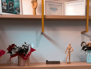 Prateleira com certificados, diplomas e quadros que comprovam a qualificação e formação da profissional da Clínica Lanna Mora