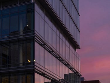 Modern architecture shot of a glass and steel building in a North American city at twilight, reflecting a deep navy and magenta sky.