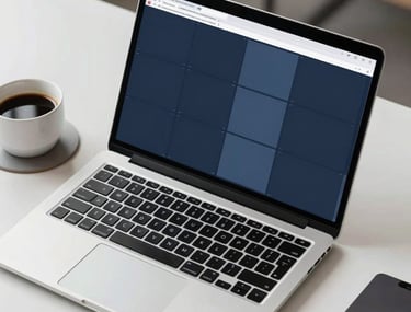 A high-angle photograph of a designer's workstation featuring a laptop with a high-resolution display. The screen shows a complex grid of dark navy and slate blue windows. Beside the laptop is a cup of black coffee on a light gray coaster. Clean, professional North American office setting.