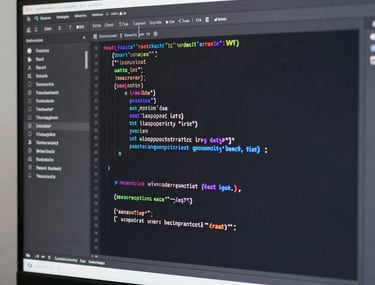 Close-up of a high-resolution monitor showing organized React code in a dark-themed editor. The lighting is neutral grey with white highlights, reflecting a clean and professional software development environment in a Turkish studio.