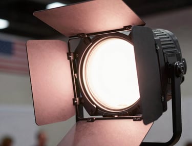 Close-up photography of a professional event lighting rig with modern fixtures glowing in a light rose pink color, soft focus on the North American / US venue background.