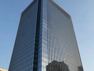 Exterior architectural rendering of a modern glass skyscraper. Sharp geometric lines against a clear blue sky. Reflective surfaces showing surrounding city architecture. Professional North American style.