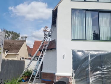 LPAD staff painting the upper exterior of a residential house white, using ladders.