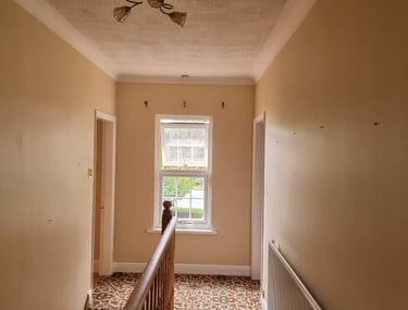 A cream-painted hallway, with a stairway leading down in a residential home.