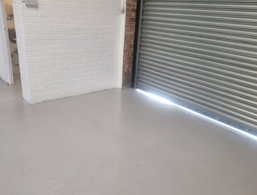A close-up of a grey floor and a painted white brick wall, next to a garage shutter door.