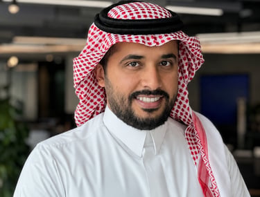 Smiling Saudi businessman wearing a traditional thobe and red shemagh in a modern office.