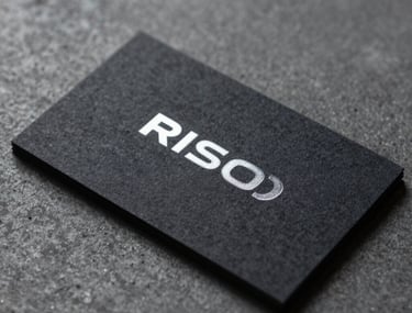 Macro photography of a sleek, dark-textured business card with silver foil lettering, resting on a charcoal gray concrete surface.