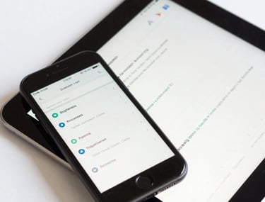 A close-up of a tablet and phone in a brightly lit studio, showing synchronized data for a business application. Clean, professional composition. Global / Western.