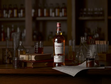 Dewars whisky bottle on a wooden table surrounded by books and glass beakers