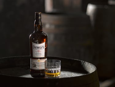 Dewars whisky bottle and glass on a wooden barrel