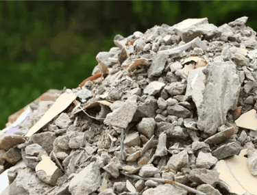 Pilha de entulho cinza com restos de concreto, tijolo e cerâmica, pronto para ser removido com caçam
