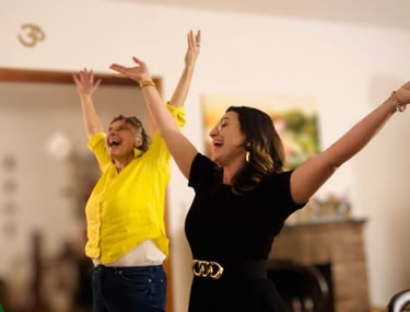 zwei Frauen lachen und singen, die Arme in der Höhe, im Hintergrund ein OM-Zeichen