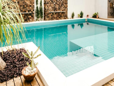 Piscina moderna no quintal com azulejos azuis, deck de madeira e arte decorativa na parede.