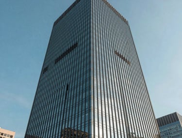 A wide shot of a modern glass skyscraper reflecting a clear blue sky, low angle, representing corporate growth and innovation. International city.