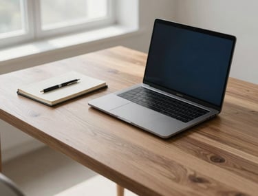A minimalist and sophisticated high-angle photograph of a modern, uncluttered workspace. The scene features a sleek laptop on a polished wooden desk, alongside a precisely organized notebook and pen. Soft, diffused natural light streams in from a large window, creating subtle shadows and highlights. The color palette is dominated by neutral tones of white, beige, and dark gray, with subtle touches of deep blue. The composition is clean and airy, conveying professionalism and calm. North American / International style.