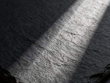 Abstract photography of light and shadow on a textured slate surface. Moody and sophisticated North American / International aesthetic.