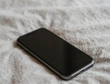 Soft focused photography of a smartphone lying face down on a light linen bedspread, morning light, indicating peace and absence of digital distraction.