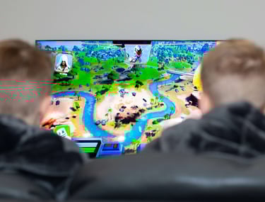 Two people playing the Fortnite video game on a large TV screen featuring a map with islands and rivers.