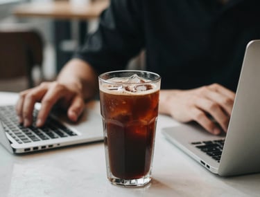 A glass of iced coffee next to a focused person's workspace in a chic Ho Chi Minh City cafe. The lighting is crisp and the vibe is productive and trendy.