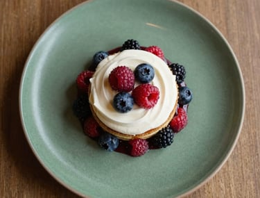 Top-down view of a stylishly plated artisanal dessert with fresh berries and cream, set on a Matte Forest Green ceramic plate. Soft, warm natural lighting, European / Iberian cafe setting.