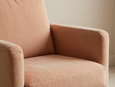 A close-up shot of a cozy reading corner with a soft salmon armchair and light beige textures. South American &amp;#x2F; Brazilian setting. Minimalist and elegant.