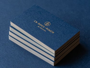 Un bodeg&oacute;n de dise&ntilde;o que muestra una colecci&oacute;n de tarjetas de visita con bordes pintados y un logotipo en relieve sobre un fondo azul oscuro profundo.