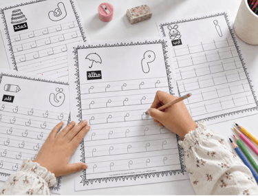 A child practicing Arabic letters on printable tracing worksheets with a pencil