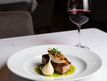A stylishly plated scandinavian dish in a cozy restaurant setting, deep red wine glass nearby, soft ambient lighting.