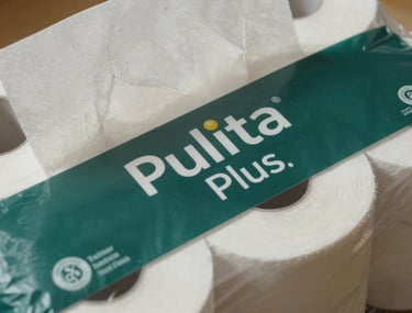 A close-up shot of Pulita Plus tissue rolls. The packaging features clean branding with dark slate green accents, emphasizing a higher quality blended feel and enhanced texture.