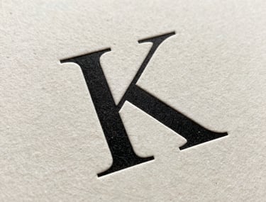 Close-up of a high-fashion serif font printed on premium thick off-white paper. Letterpress texture visible. Minimalist and elegant.