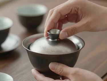 Close-up of two hands performing a traditional tea ceremony ritual, emphasizing precision and grace. Soft, natural lighting on silver and charcoal ceramic.