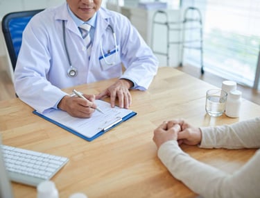 A doctor in a white coat consulting with a patient and writing medical notes on a clipboard.