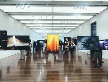 Pessoa admirando uma pintura em uma galeria de arte com iluminação suave e obras em exibição ao fund