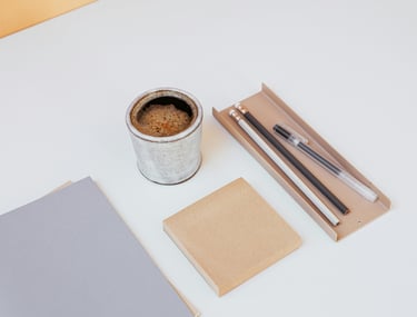 Minimalist desk workspace with a ceramic espresso cup, notebook, and stationery on a white surface.