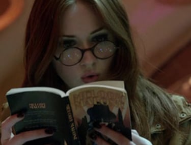 a woman in glasses and a jacket is reading a book