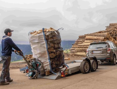 ein mitarbeiter fährt ein Big Bag voll mit brennholz auf einen Autoanhänger um ihn auszuliefern
