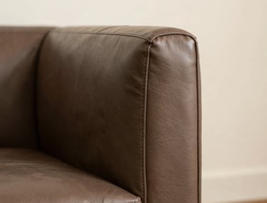 Close-up architectural photography of high-quality leather furnishings in a South Asian / Indian luxury office. The texture of the muted brown leather is detailed, set against an off-white backdrop with soft, warm light.