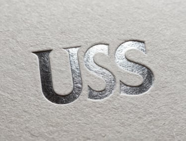 Detailed shot of a textured paper surface with a sharp, silver foil embossed logo under bright studio lighting, sophisticated and premium, North American / US.