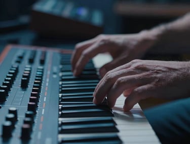 Cinematic close-up of a person's hands adjusting a modern synthesizer interface in a dimly lit North American studio, deep blue and muted blue color palette.