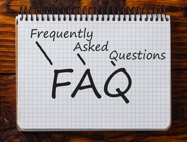 Handwritten FAQ acronym for Frequently Asked Questions on a spiral notebook with a wood background.