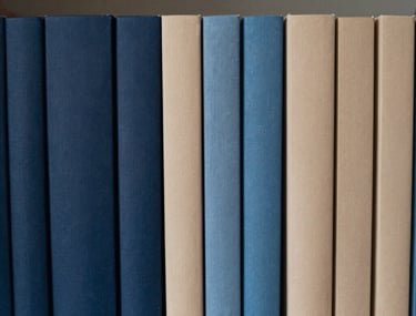 A row of journals lined up on a shelf, showing a gradient of blues and beiges. The shot is minimalist and calm, emphasizing order and curation. Southeast Asian context.